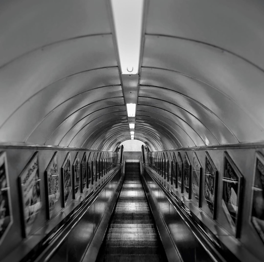 Black and white photo of an empty escalator in a tunnel-like setting.