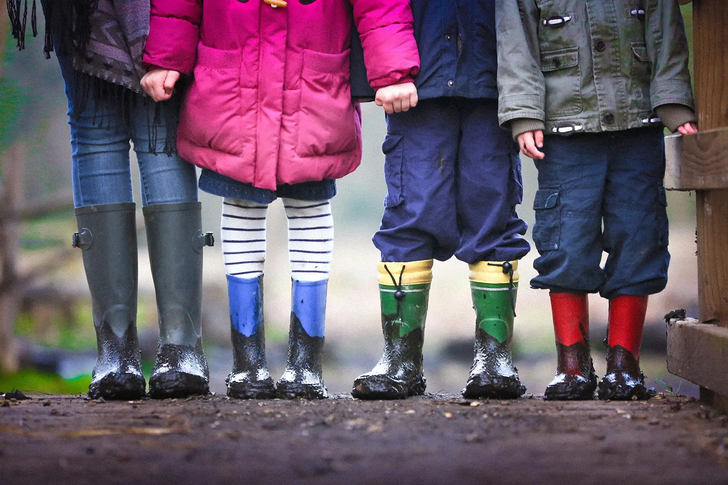 Children wearing colorful rain boots standing side by side.