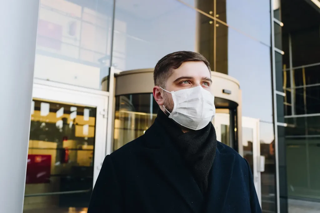 Man wearing a face mask outdoors near a building.