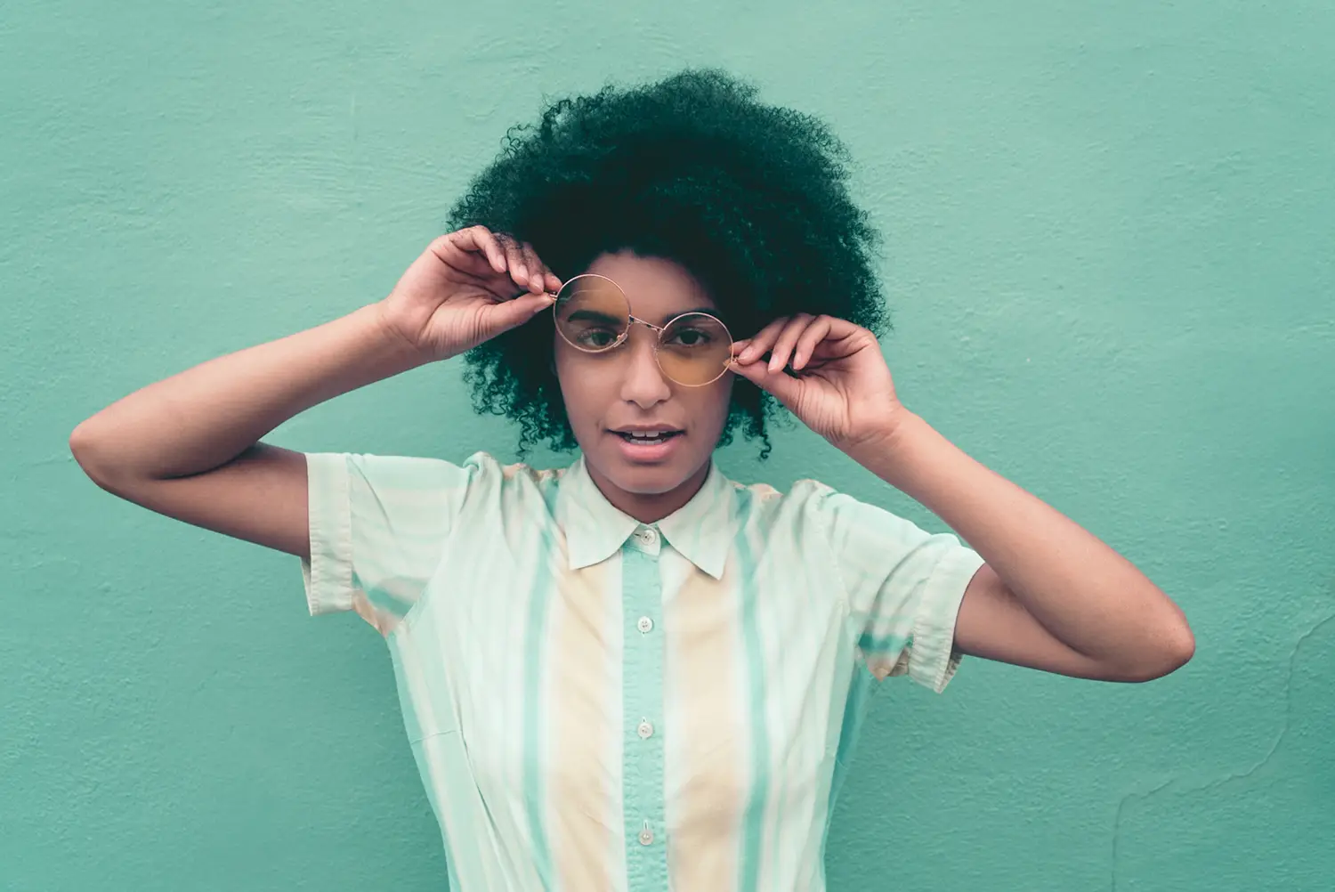 Person adjusting sunglasses against a green background.